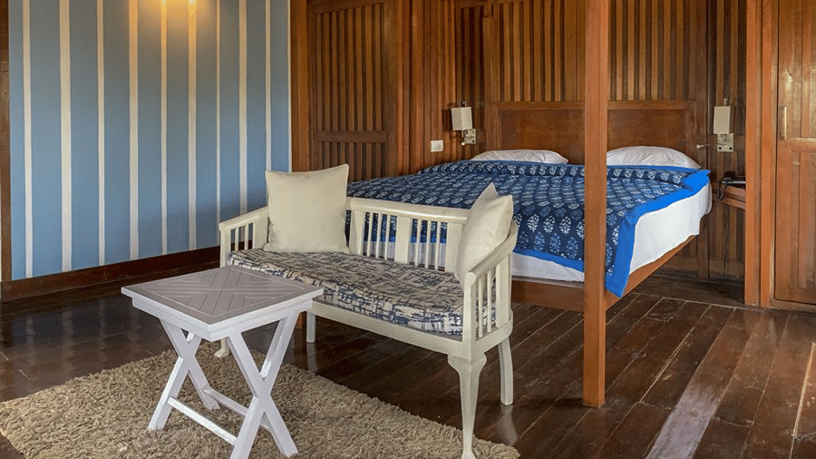 King size bed with blue bedding and a small white seating area in a wood-panelled room.