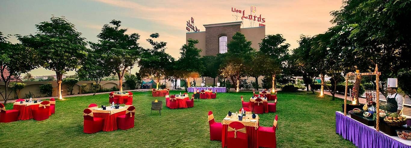 An outdoor area is prepared for an event with tables covered in red cloths on the grass - Lion Lords Inn Rajula