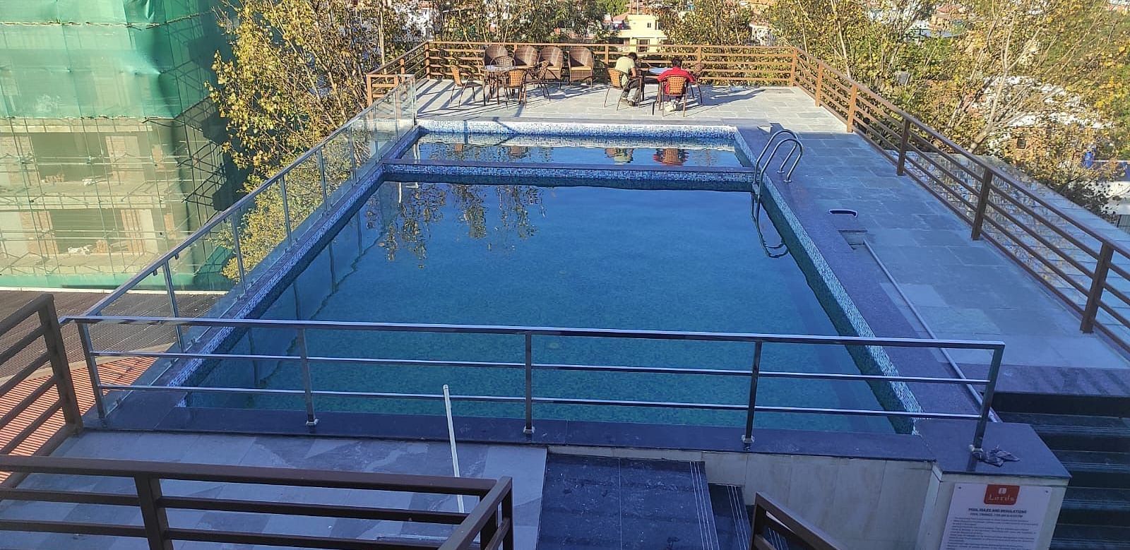 The swimming pool with clear water and a pool patio covered by safety railing and seating chairs at Two spa tables placed in a room with carpeted flooring, curtained windows, a chair and a table at Mandala Norling Lords Prime in Kathmandu.