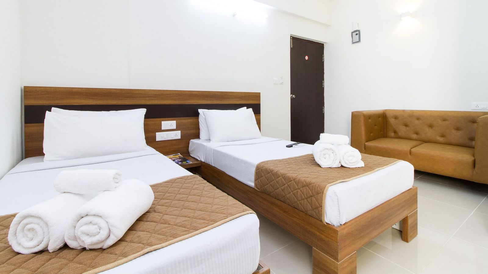 A room at Sanctum Suites Whitefield, Bangalore including twin beds with brown and white bedding and a sofa.