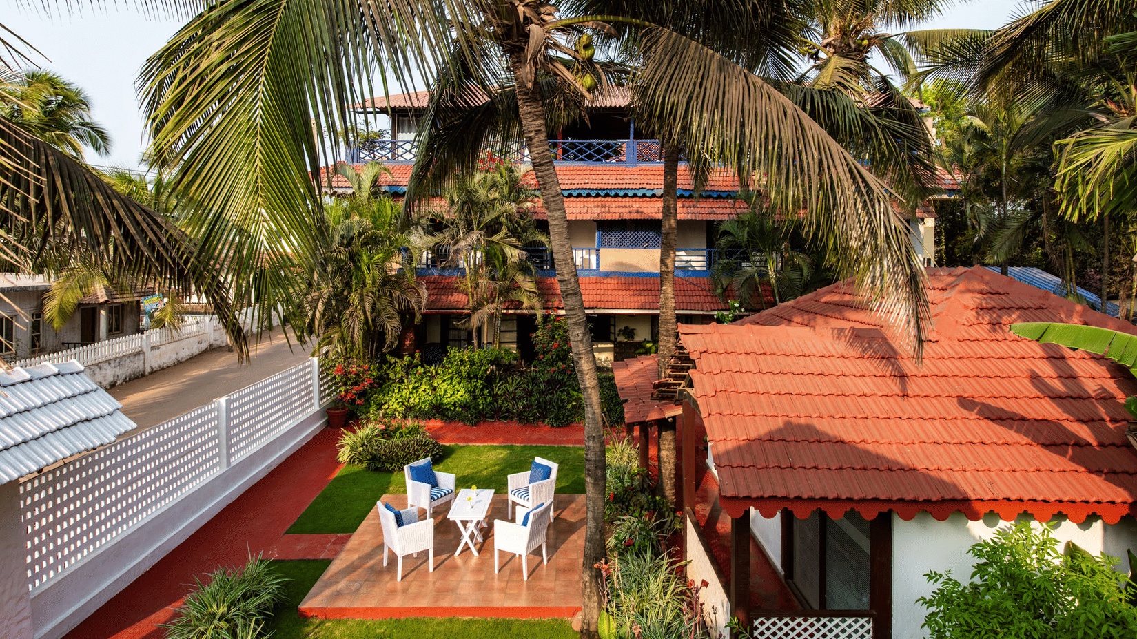 Elevated view of red-roofed cottages, palm trees, garden seating and a swimming pool.