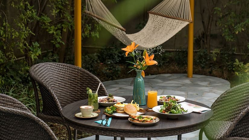 A table laid out with different dishes and also a flower vase kept for decoration in the Karma Chalet amidst lush greenery - Karma Lakelands.