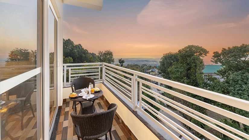 a balcony with two chairs and a table kept in the centre with mountain views - Stone Wood Mountain Resort, Dharamshala