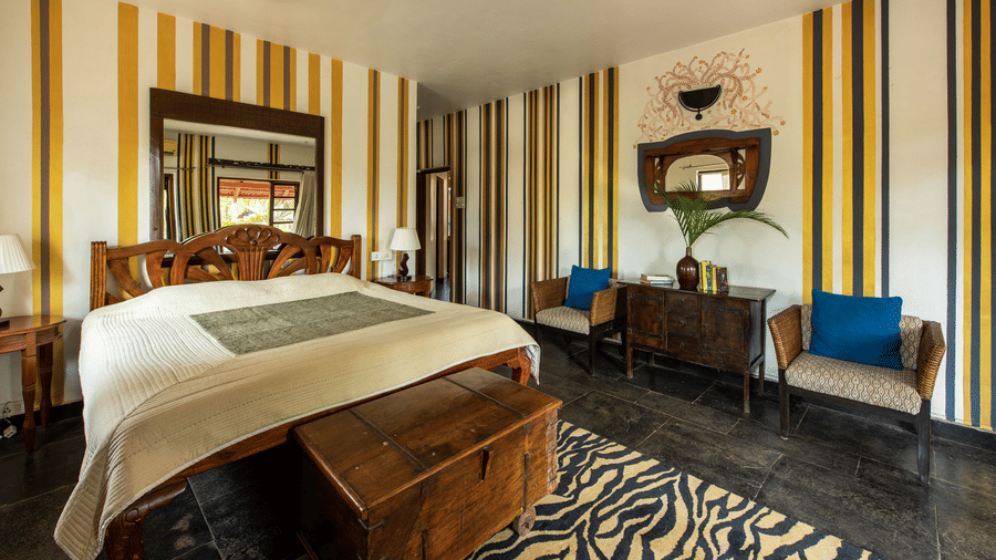 Spacious bedroom with a king size bed, striped walls, wooden furnishings and blue accent chairs.