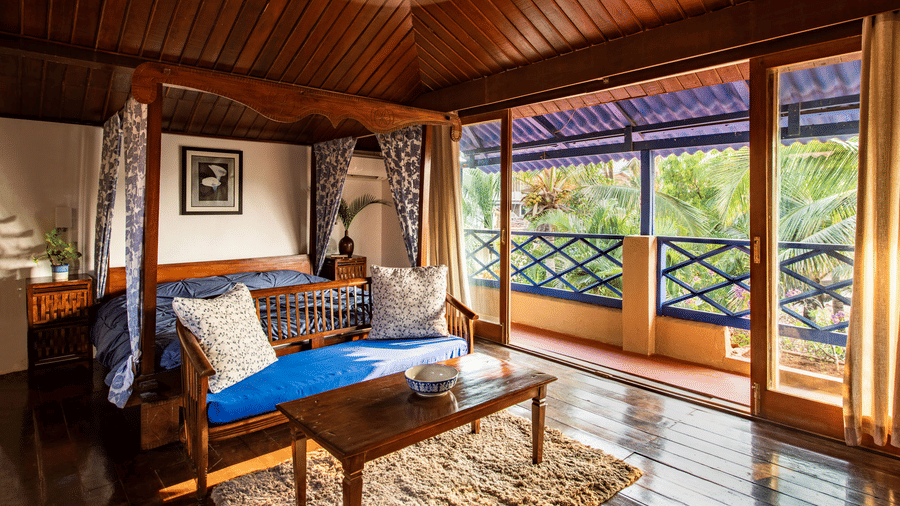 Wooden room with a seating area, blue-cushioned chairs, coffee table and a covered balcony overlooking greenery.