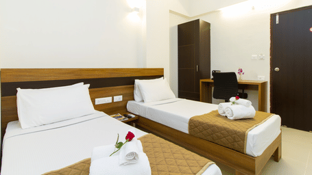 Twin bedroom with two beds, white linen, a dark wooden wardrobe, and a red rose accent at Sanctum Suites Whitefield, Bangalore.