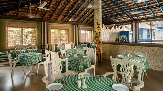 Covered dining area with green checked tablecloths, white chairs and tables beneath a traditional tiled roof.
