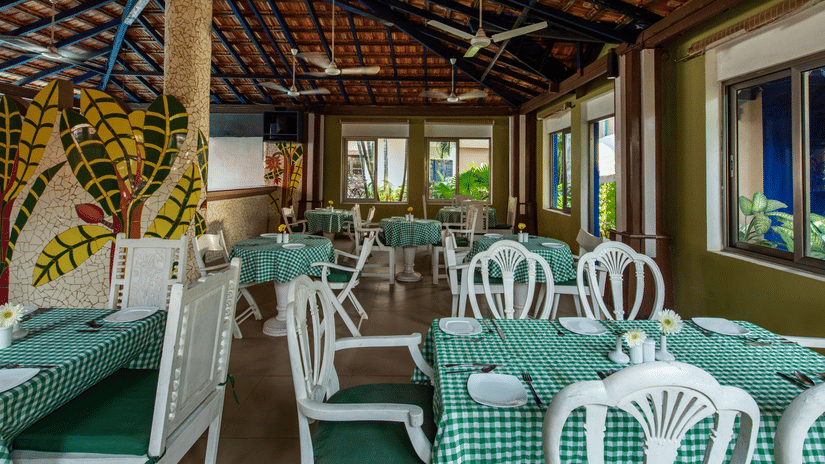 Open-air dining space with green checked tablecloths, white chairs and large windows overlooking greenery.