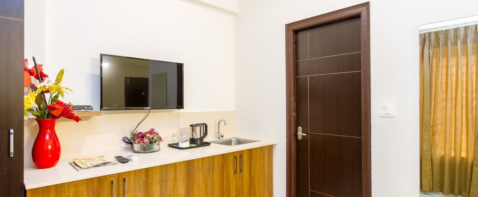 A hotel room showing wooden cabinets, including a television, and a door at Sanctum Suites Whitefield, Bangalore.