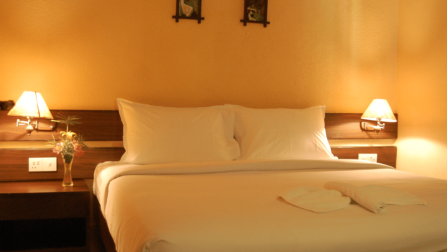 Premium suite with king size bed, bedside tables with lamps, yellow painted walls, framed art, and bottled water at Green Pastures, Kodaikanal.