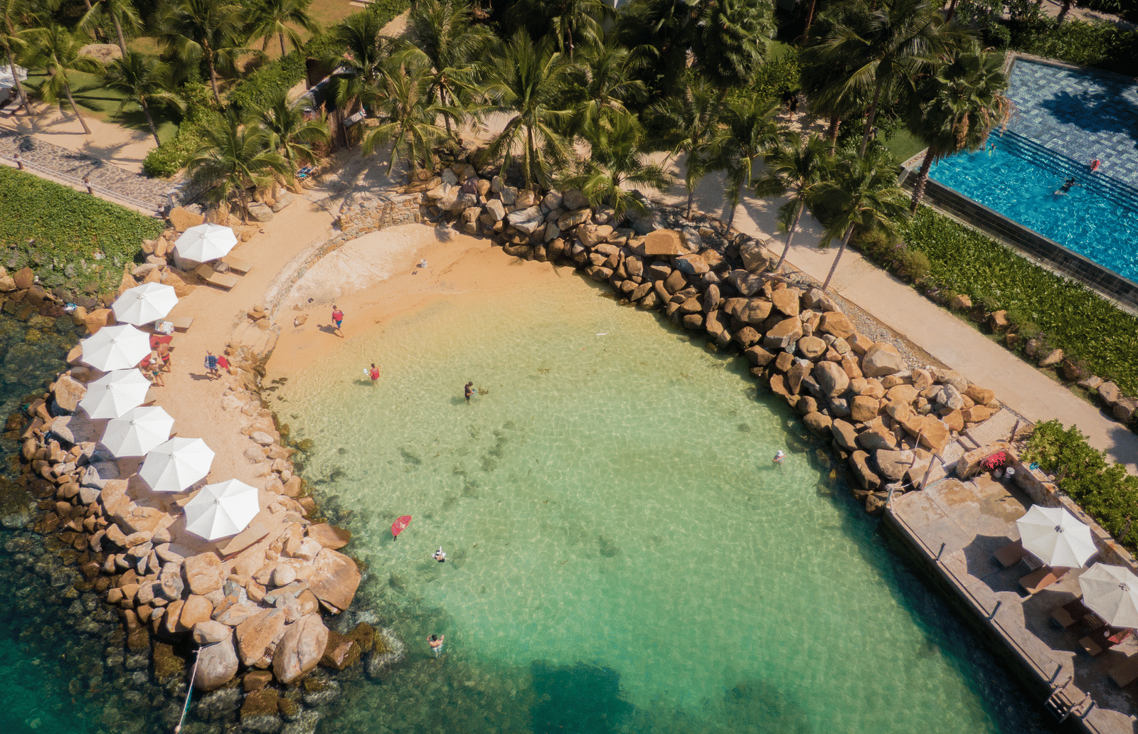 A private beach at Alibu Resort Nha Trang featuring lounger beds with umbrellas, people swimming, or resting.