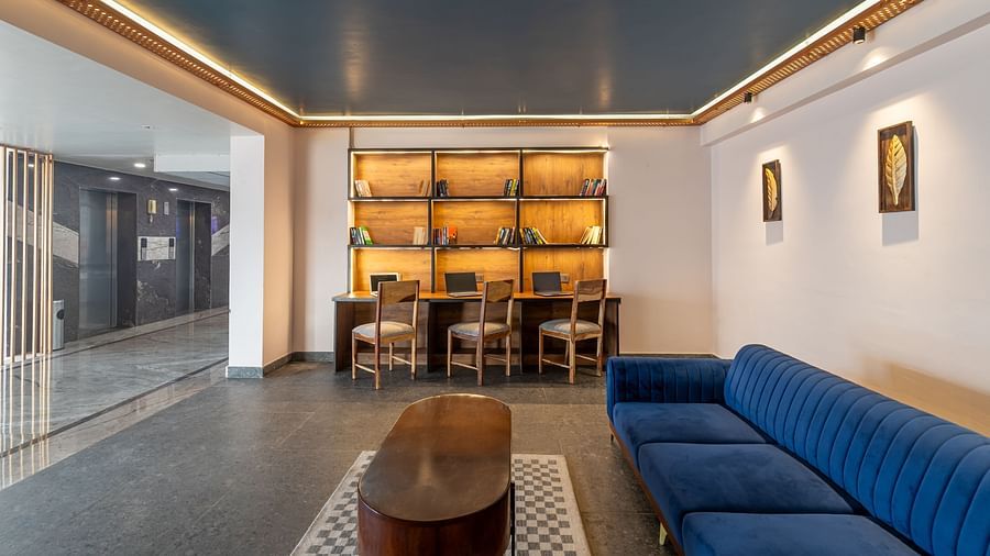 Lobby area of Clarks Inn Suites Jaipur, Ajmer Road featuring a three-seater sofa of navy blue colour with a wooden coffee table and a workstation in the background