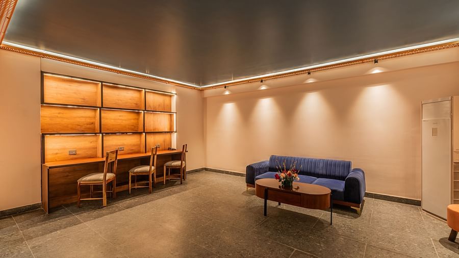 A warmly lit lobby of Clarks Inn Suites Jaipur, Ajmer Road featuring a three-seater sofa with a coffee table and a workstation beside it with plug point and three chairs