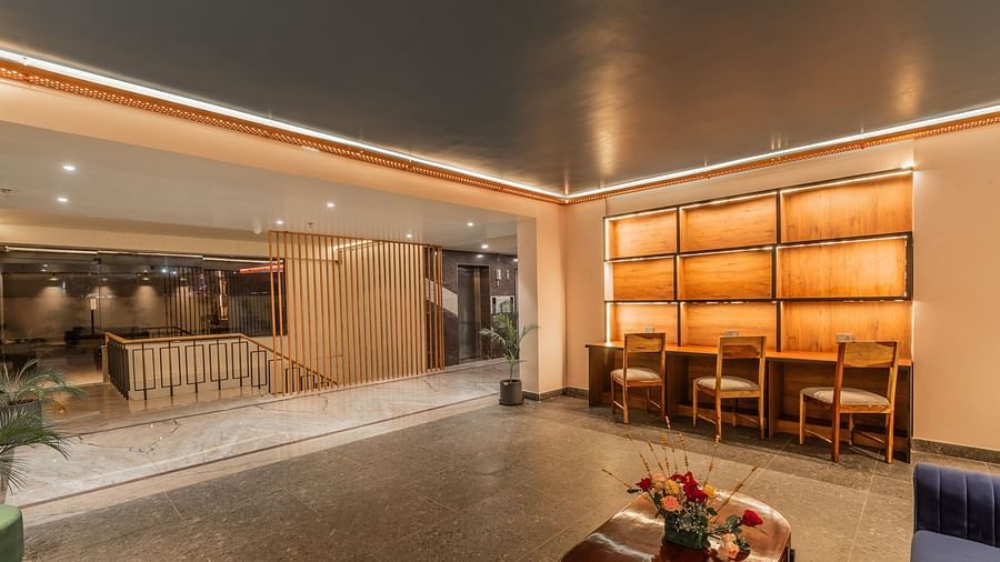 A well-lit lobby area at Clarks inn Suites jaipur, Ajmer Road featuring a staircase beside which is a desk with shelves and plug points and three chairs