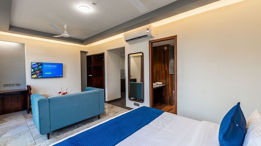 Deluxe King Room at Clarks Inn Suites Jaipur featuring a plush king bed with blue accents, a comfortable seating area, a wall-mounted TV, a mirror, and soft ambient lighting