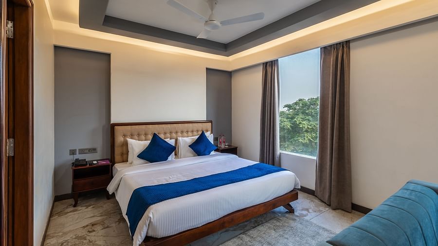 Deluxe King Room at Clarks Inn Suites Jaipur with a king size bed, blue accents, large window, cosy seating, warm lighting and elegant modern decor