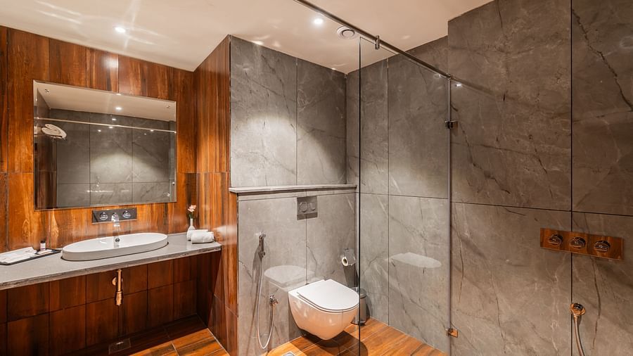 Deluxe King Room at Clarks Inn Suites Jaipur featuring a spacious bathroom with a modern design, including a wall-mounted toilet, sleek countertop basin, large mirror, and a glass-enclosed shower area with elegant lighting