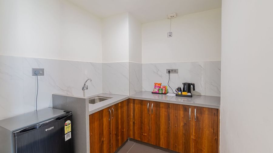 Compact kitchenette with wooden cabinets, stainless steel sink, mini fridge, tiled backsplash, and essential appliances for convenient self-catering accommodation at Clarks Inn Suites Jaipur