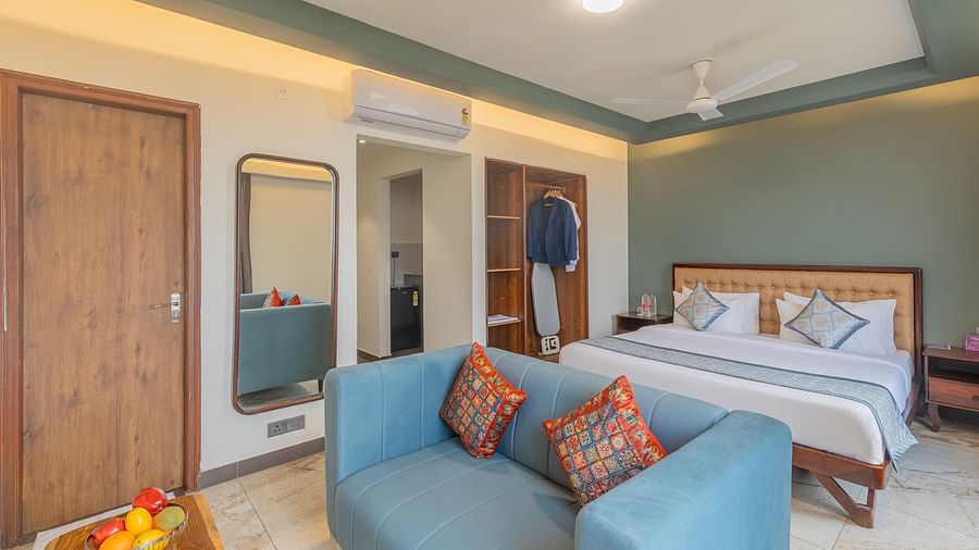 Deluxe King Room at Clarks Inn Suites Jaipur featuring king size bed, blue sofa, wooden furniture, wardrobe, mirror, air conditioning, and warm lighting for comfort