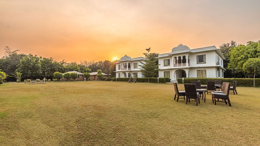 A view of Clarks Inn Suites, Ranthambore with a lawn and seating area in the foreground and a sunset in the background.