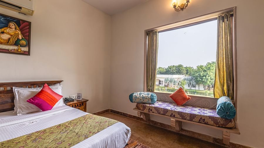 A guest room at Clarks Inn Suites, Ranthambore with a comfortable bed and a seating area overlooking the resort grounds.