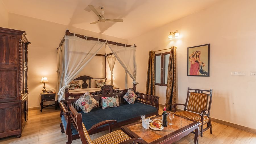 A spacious and inviting room at Clarks Inn Suites, Ranthambore, featuring a four-poster bed, a seating area, and traditional decor.