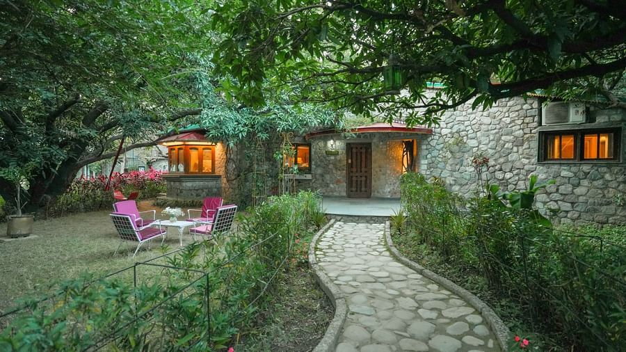 An outdoor garden with a stone pathway, plants, and a building with lit windows at night - The Den Corbett Resort & Spa, Kumeria.