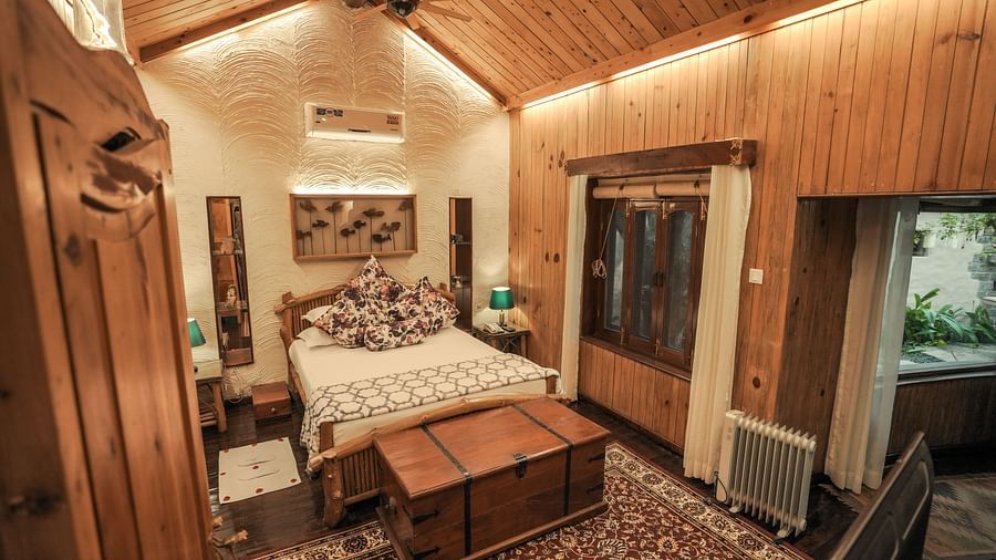 A bedroom with a bed, a wooden chest, and a patterned rug, warm lighting - The Den Corbett Resort & Spa, Kumeria.
