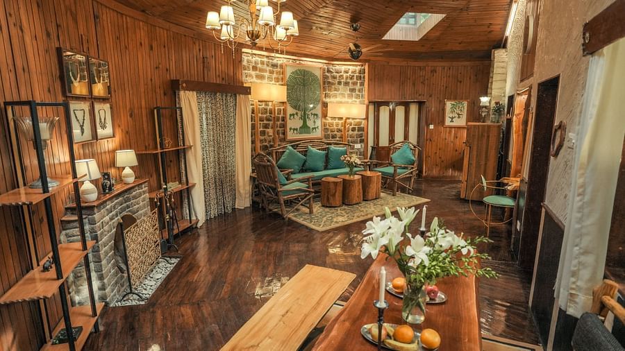 A living room with a wooden table, chairs, and a chandelier, warm lighting - The Den Corbett Resort & Spa, Kumeria.