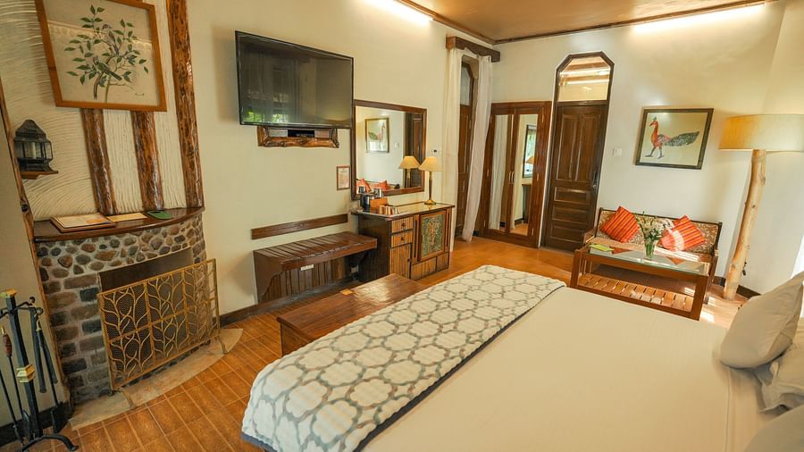 A bedroom with a bed, a television, and warm lighting, wooden interior - The Den Corbett Resort & Spa, Kumeria.