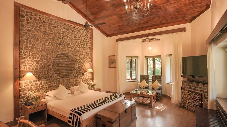 A bedroom with a bed, a patterned rug, and warm lighting, wooden interior - The Den Corbett Resort & Spa, Kumeria.
