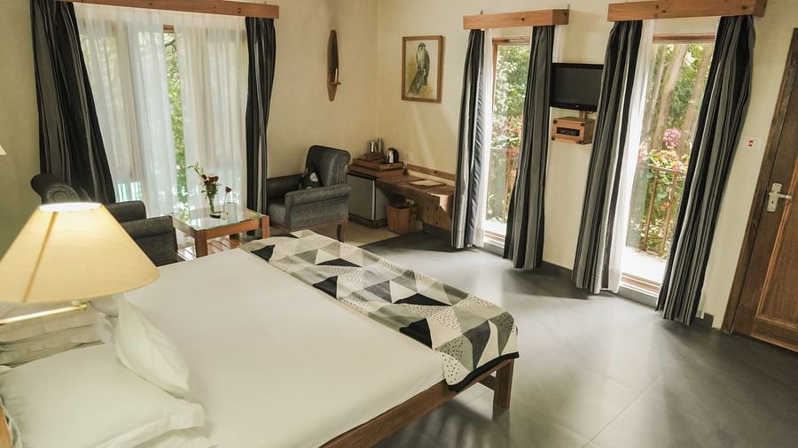 A living room with a couch, chairs, and a view of a garden - The Den Corbett Resort & Spa, Kumeria.