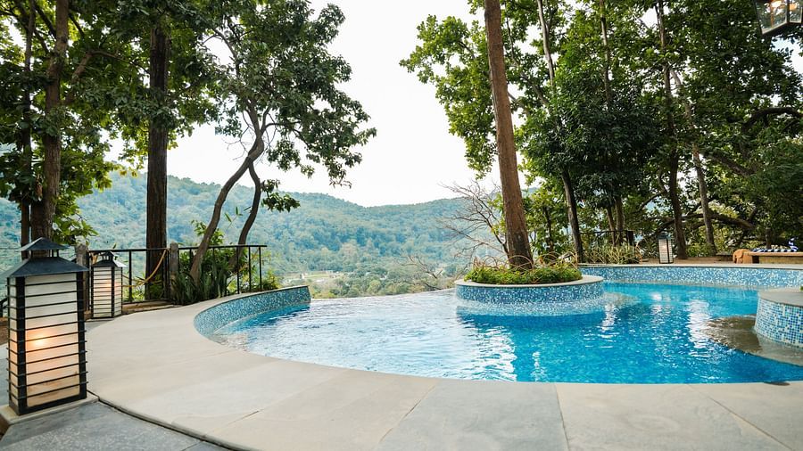 A swimming pool overlooking a valley with trees and mountains, daytime setting.