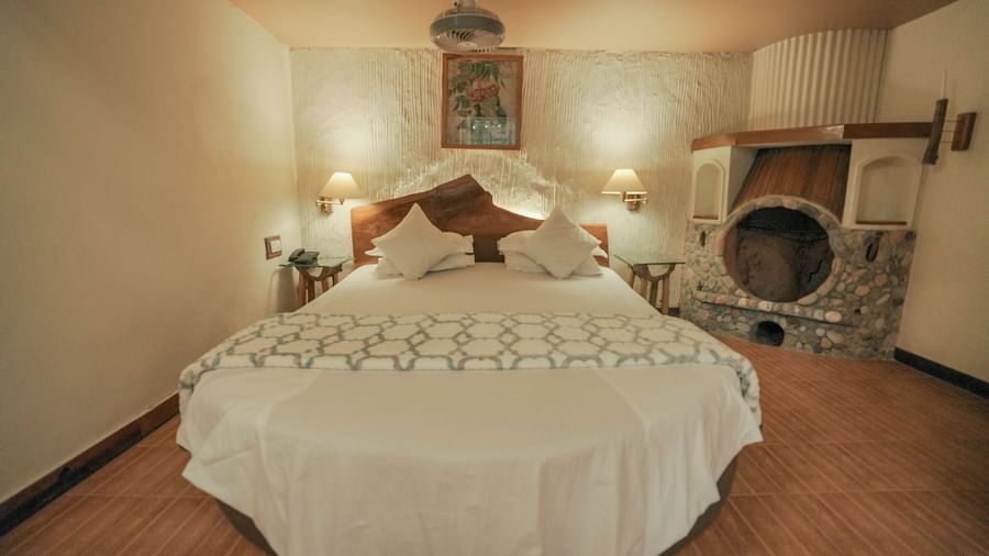 A bedroom with a white bed, a rug, and warm lighting, interior setting - The Den Corbett Resort & Spa, Kumeria.