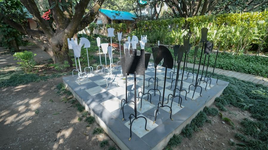 A modern art installation with reflective surfaces in a garden setting, surrounded by trees.