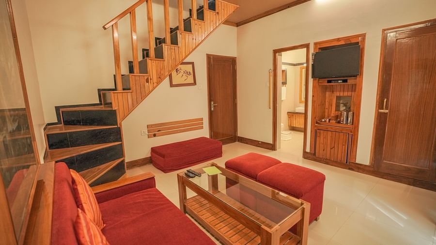 A living room with a couch, stairs, and warm lighting, wooden interior - The Den Corbett Resort & Spa, Kumeria.