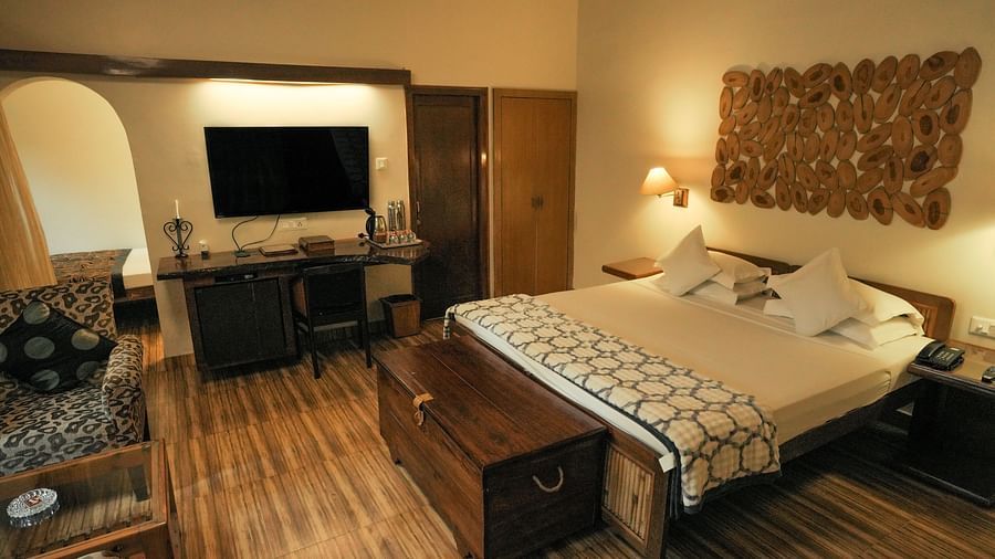 A bedroom with a bed, a television, and warm lighting, wooden interior - The Den Corbett Resort & Spa, Kumeria.