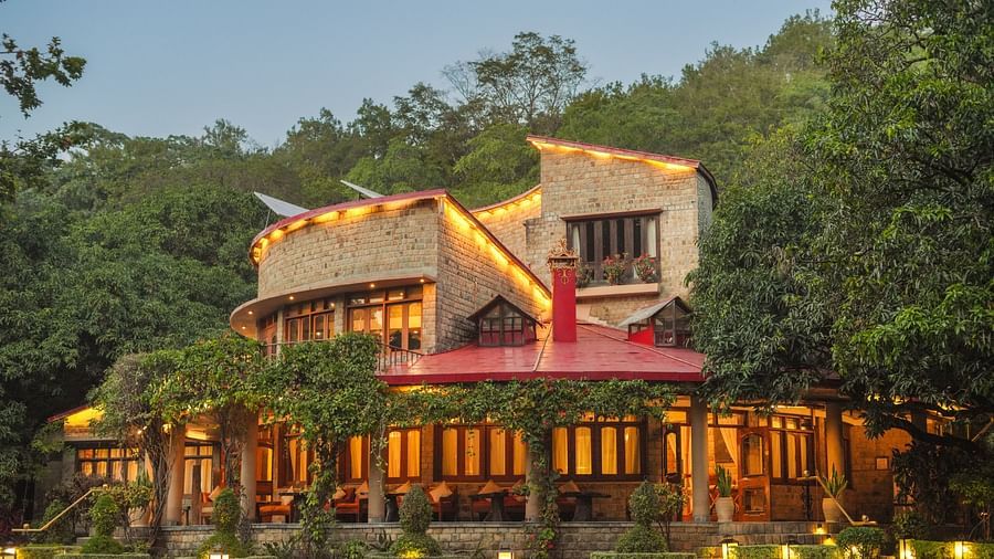 A multi-level building with lights, nestled in a forested hillside at dusk.
