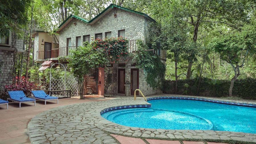 A building with a swimming pool and lounge chairs, surrounded by trees.