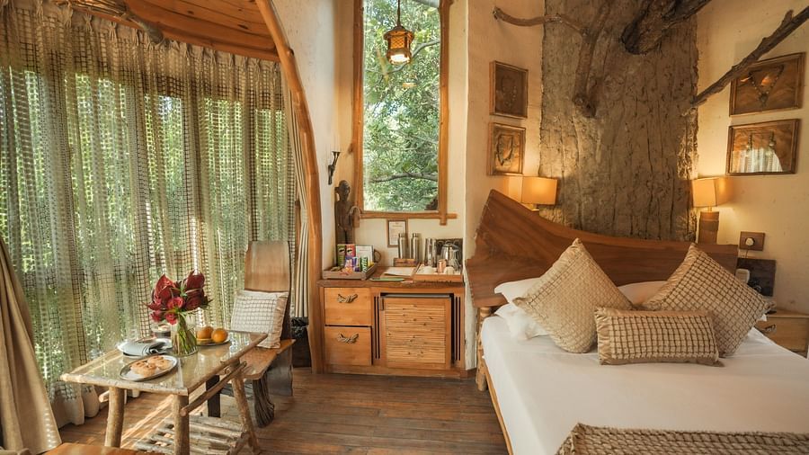 A bedroom with a bed, a lamp, and warm lighting, large windows - The Den Corbett Resort & Spa, Kumeria.