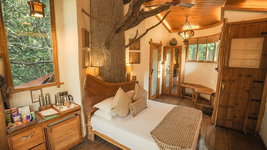 A bedroom with a bed, a lamp, and warm lighting, interior setting with wooden elements and large windows - The Den Corbett Resort & Spa, Kumeria.