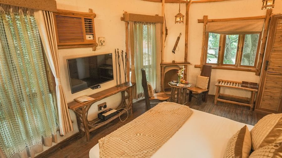 A bedroom with a bed, a television, and warm lighting - The Den Corbett Resort & Spa, Kumeria.