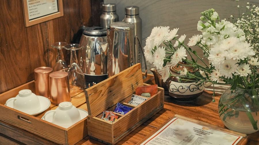 A table with various items, including a plant, boxes, and a metal container, warm lighting - The Den Corbett Resort & Spa, Kumeria.