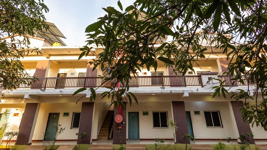 A low angle view of the facade featuring brown and beige multi-storey building surrounded by greenery at Daksh Resort & Amusement Park, Sasan Gir.