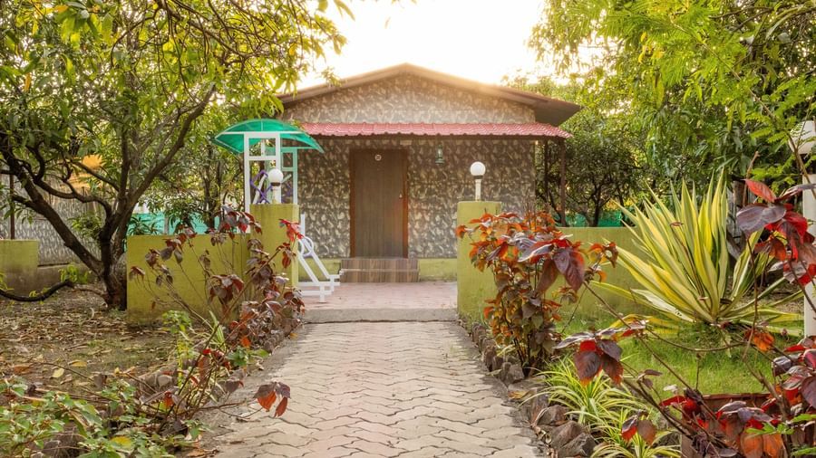 An outdoor view of a small red-roofed cottage with a winding path and green landscaping, at Daksh Resort & Amusement Park, Sasan Gir.