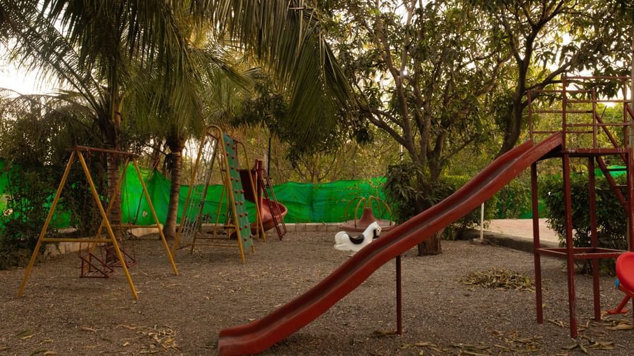 An outdoor children's play area with green swings and a red slide at Daksh Resort & Amusement Park, Sasan Gir.
