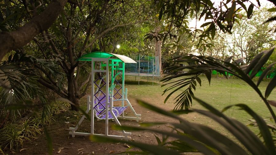 A white and green swing set on green grass, surrounded by trees at Daksh Resort & Amusement Park, Sasan Gir.