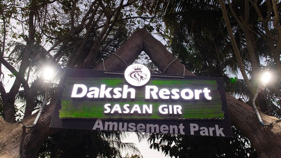 An illuminated sign of Daksh Resort & Amusement Park, Sasan Gir, visible at dawn among trees.