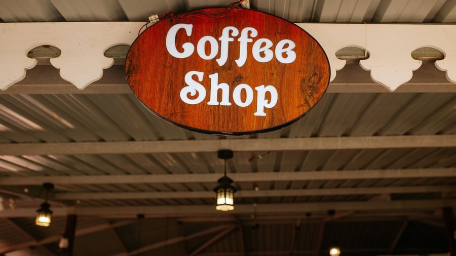 A close-up of the rustic, wooden sign reading Coffee Shop hanging under a metal roof, at Daksh Resort & Amusement Park, Sasan Gir.