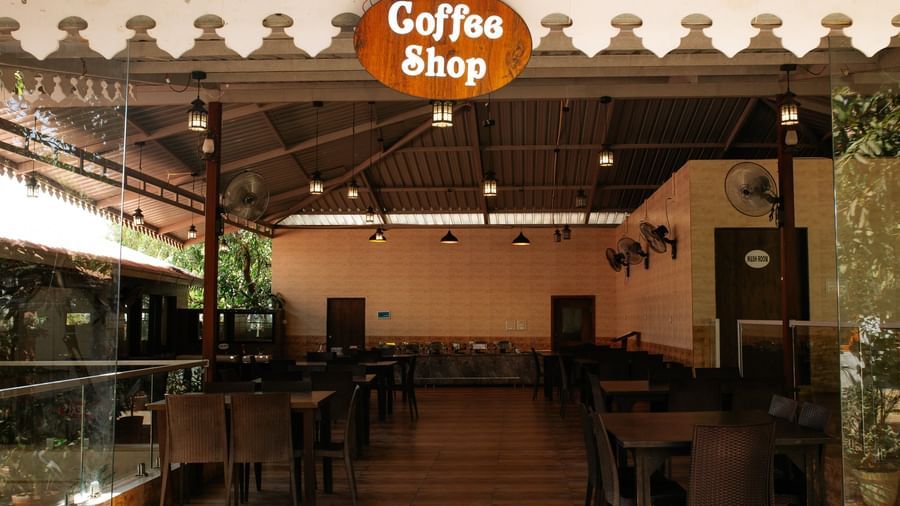A view of the dark, empty Coffee Shop area with black tables and a glass railing, at Daksh Resort & Amusement Park, Sasan Gir.
